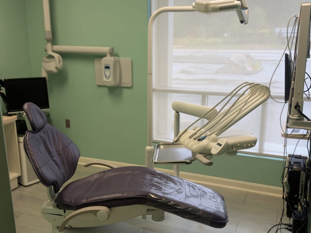 A treatment room: the dental chair beside a large window, with the imaging screen and instruments within reach