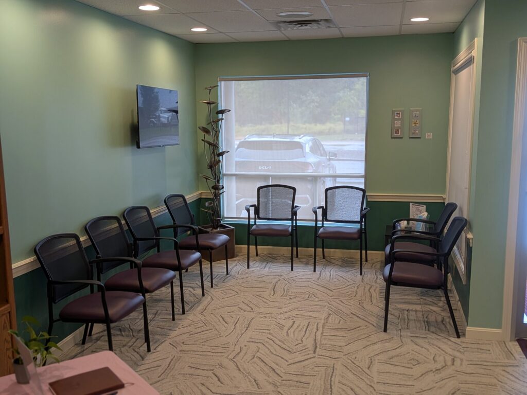 The waiting room at Cedars Family Dental: chairs along sage-green walls, a window onto the parking area and a shelf of patient information