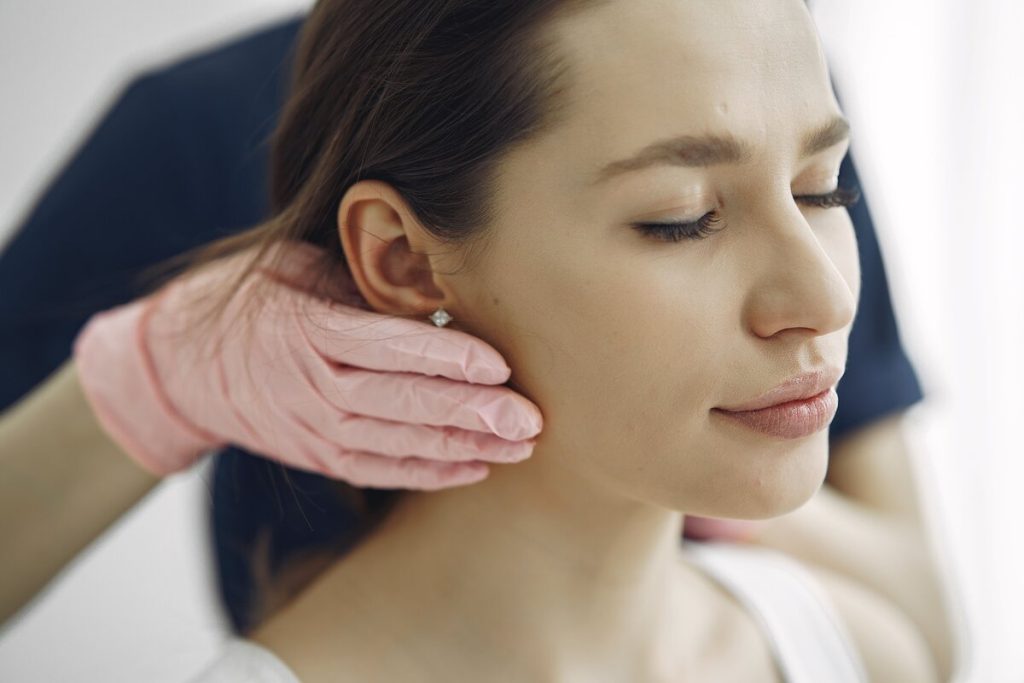 A gloved hand rests on a relaxed woman's jaw muscle below her ear