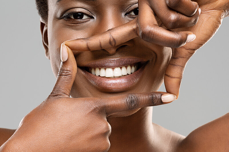 A smiling woman frames her white teeth with her fingers
