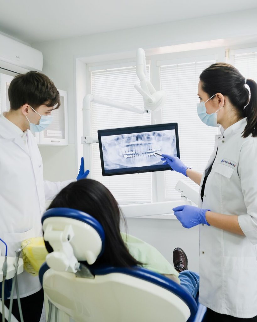 A dentist and an assistant review an x-ray on the screen beside a patient in the chair