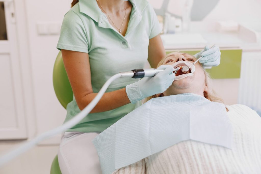 A hygienist cleans a reclining patient's teeth with an ultrasonic scaler