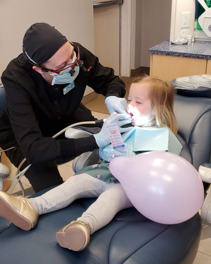 A young girl holding a pink balloon reclines in the dental chair during her checkup