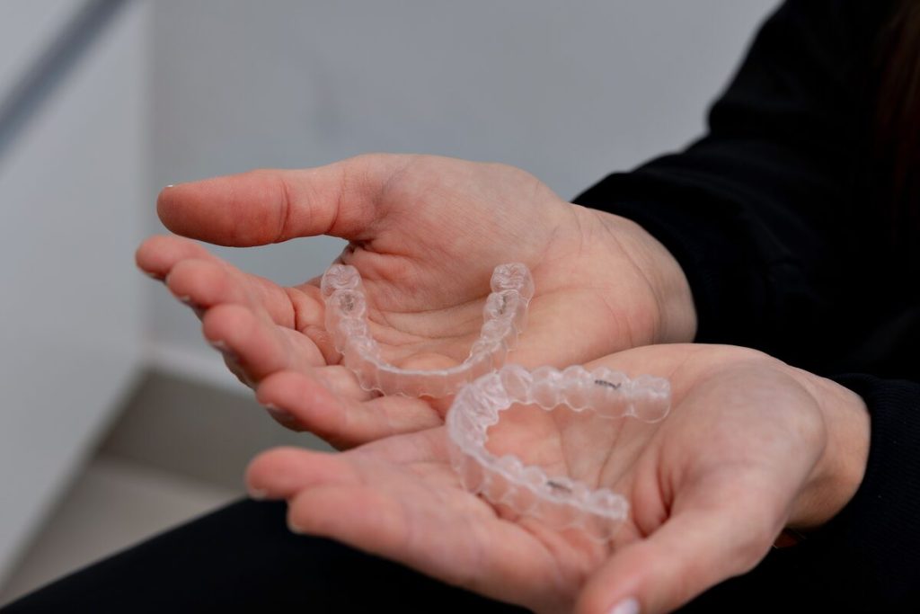 A pair of clear aligners held in open hands