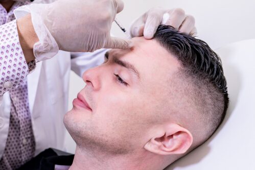 A patient reclines with eyes closed while a gloved provider gives an injection in the forehead